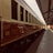 A vintage train carriage with a note indicating it as first class is stationed on the tracks of a covered train platform. The carriage has a classic design, characterized by its maroon and beige color scheme and large, rectangular windows. The platform is lined with a metal roof supported by beams, offering shade to the boarding area.