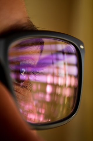 An eye is reflected in the lens of glasses, with a grid of purple and pink lights creating a pattern over the lens surface.