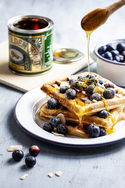 person putting honey on waffle with blueberry fruits