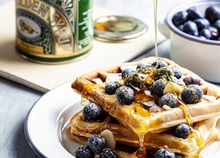 person putting honey on waffle with blueberry fruits