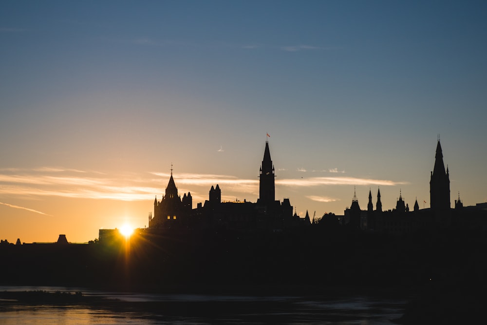 silhouette of houses and tower near river during sunrise