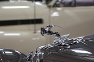 Close-up of a classic car hood ornament gleaming under showroom lights.