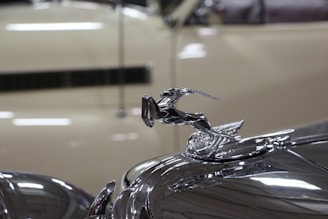 Close-up of a classic car hood ornament gleaming under showroom lights.