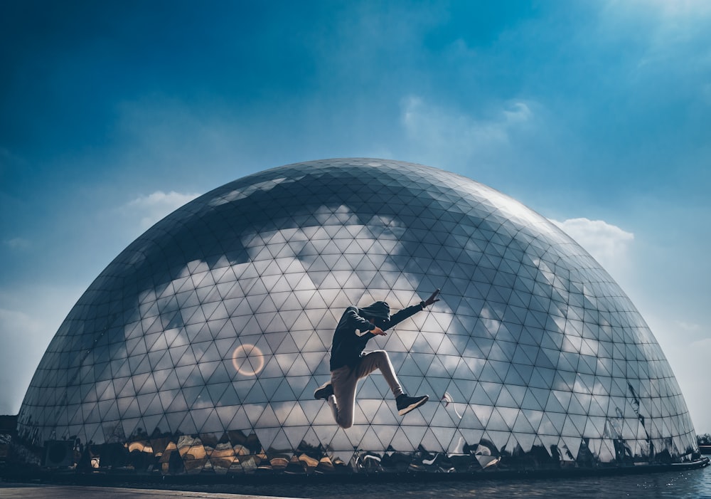 man jumping in front of dome mirror building under blue sky
