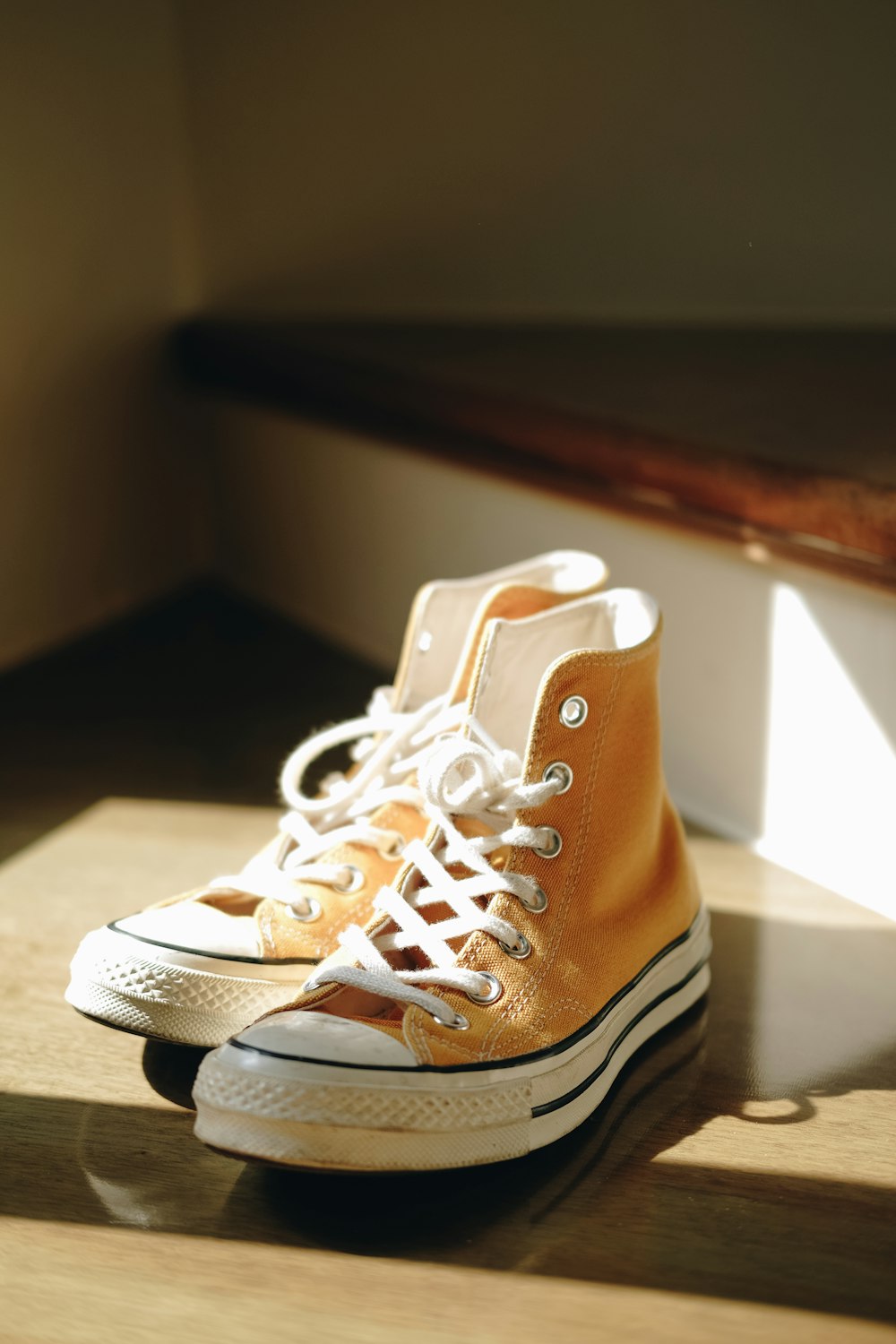 yellow-and-white Converse All-Star high-top sneakers on brown wooden staircase