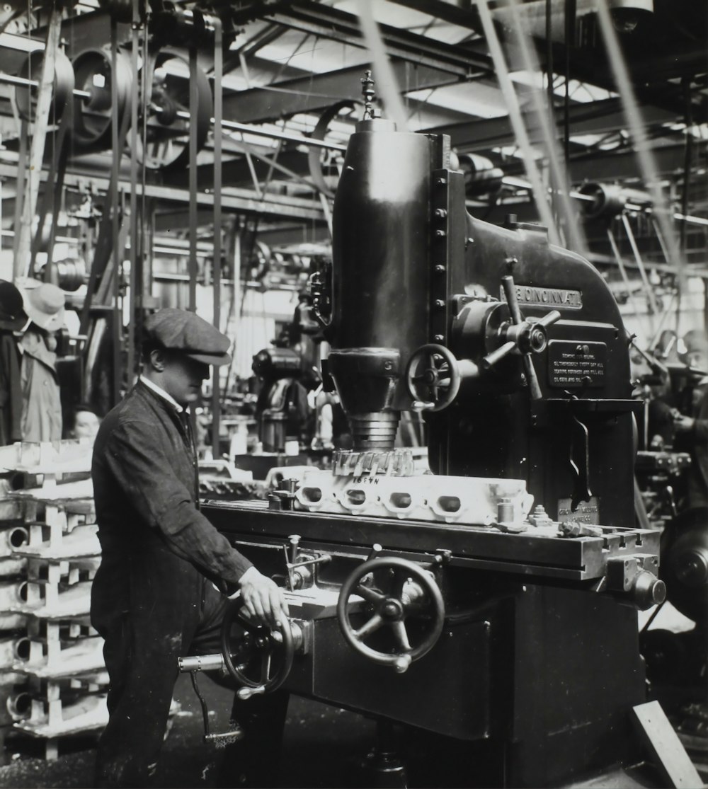 Fotografía en escala de grises del hombre frente a una máquina mecánica