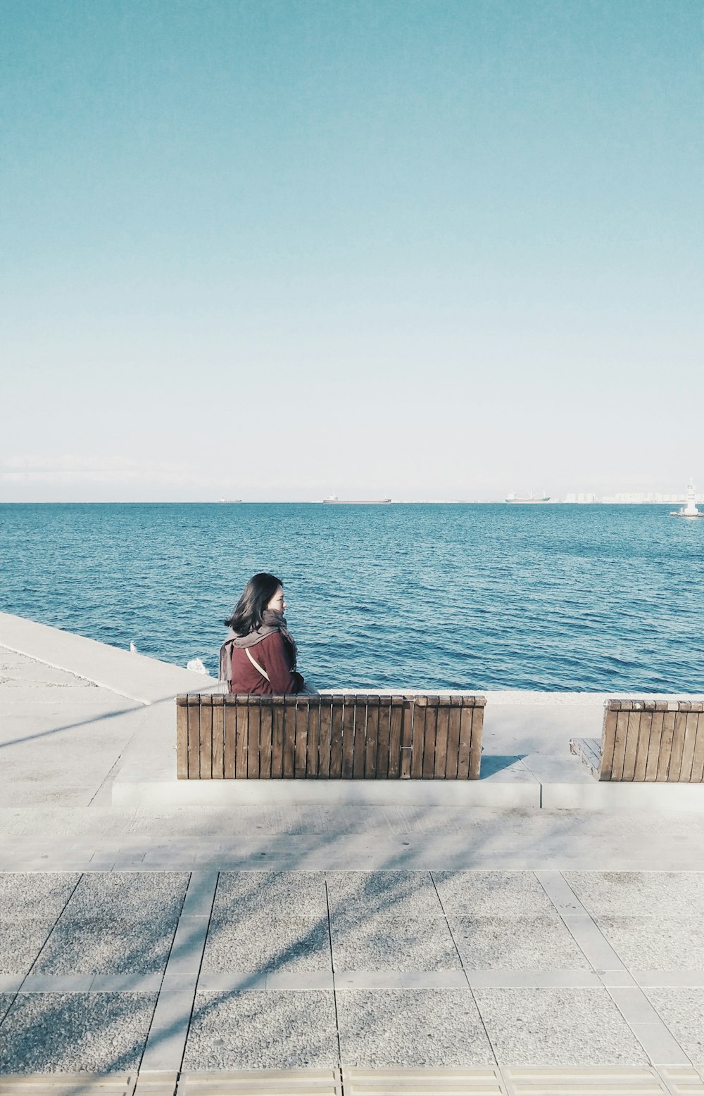 woman sitting on bench facing ocean