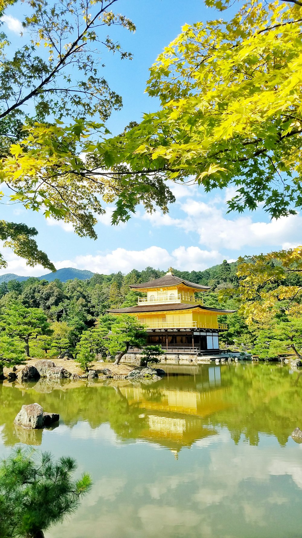 yellow temple facing body of water surrounded with trees