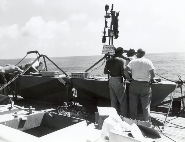 Technician operating side scan sonar equipment on deck with offshore platform visible in the background