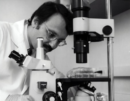 grayscale photography of doctor using microscope