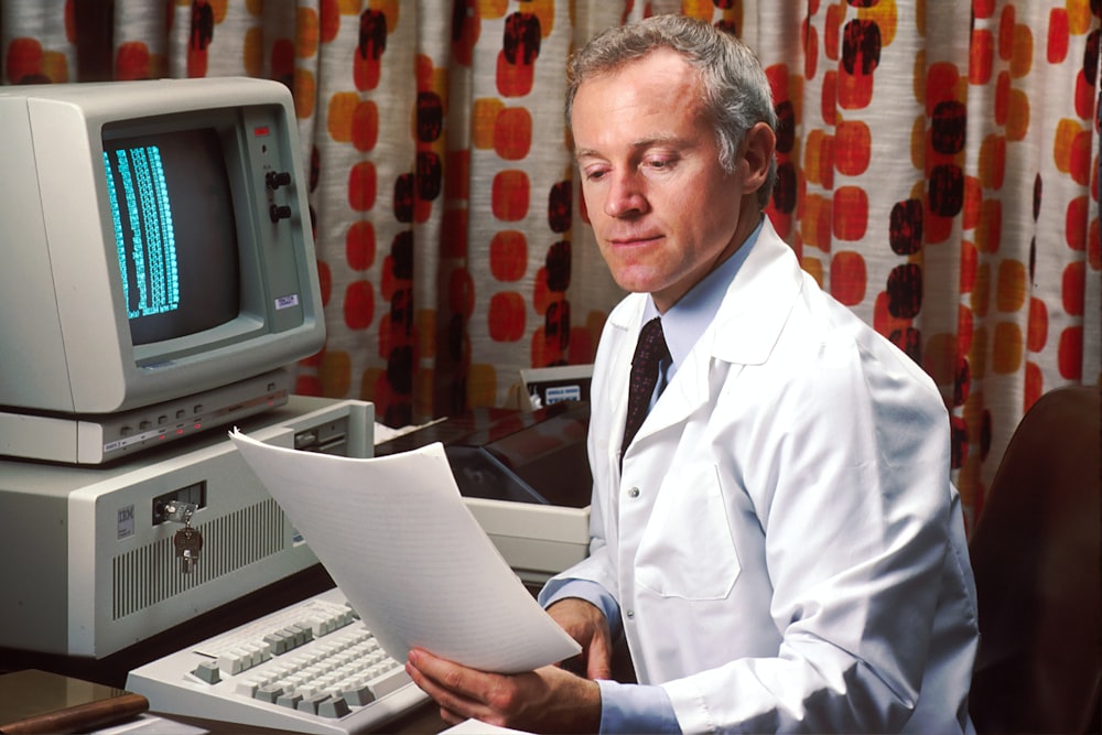 hombre leyendo papeles frente a una computadora. Imagen vintage