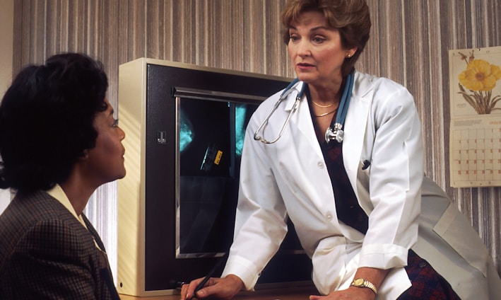 doctor sitting on desk talking to sitting woman