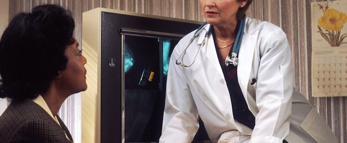 doctor sitting on desk talking to sitting woman