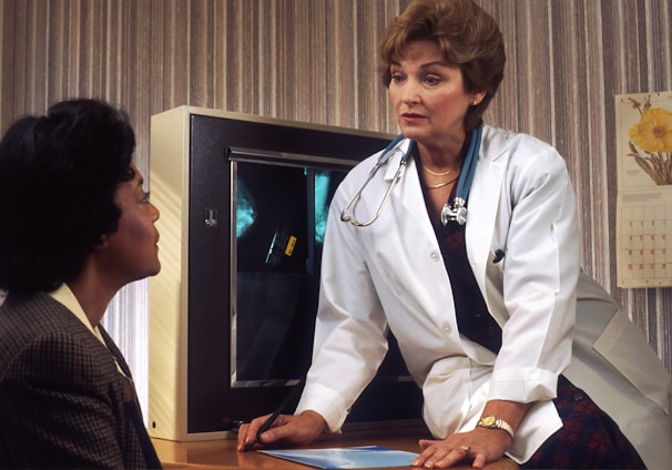 doctor sitting on desk talking to sitting woman