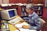 A smiling middle-aged woman sitting at her kitchen table, confidently filling out probate forms on a laptop.