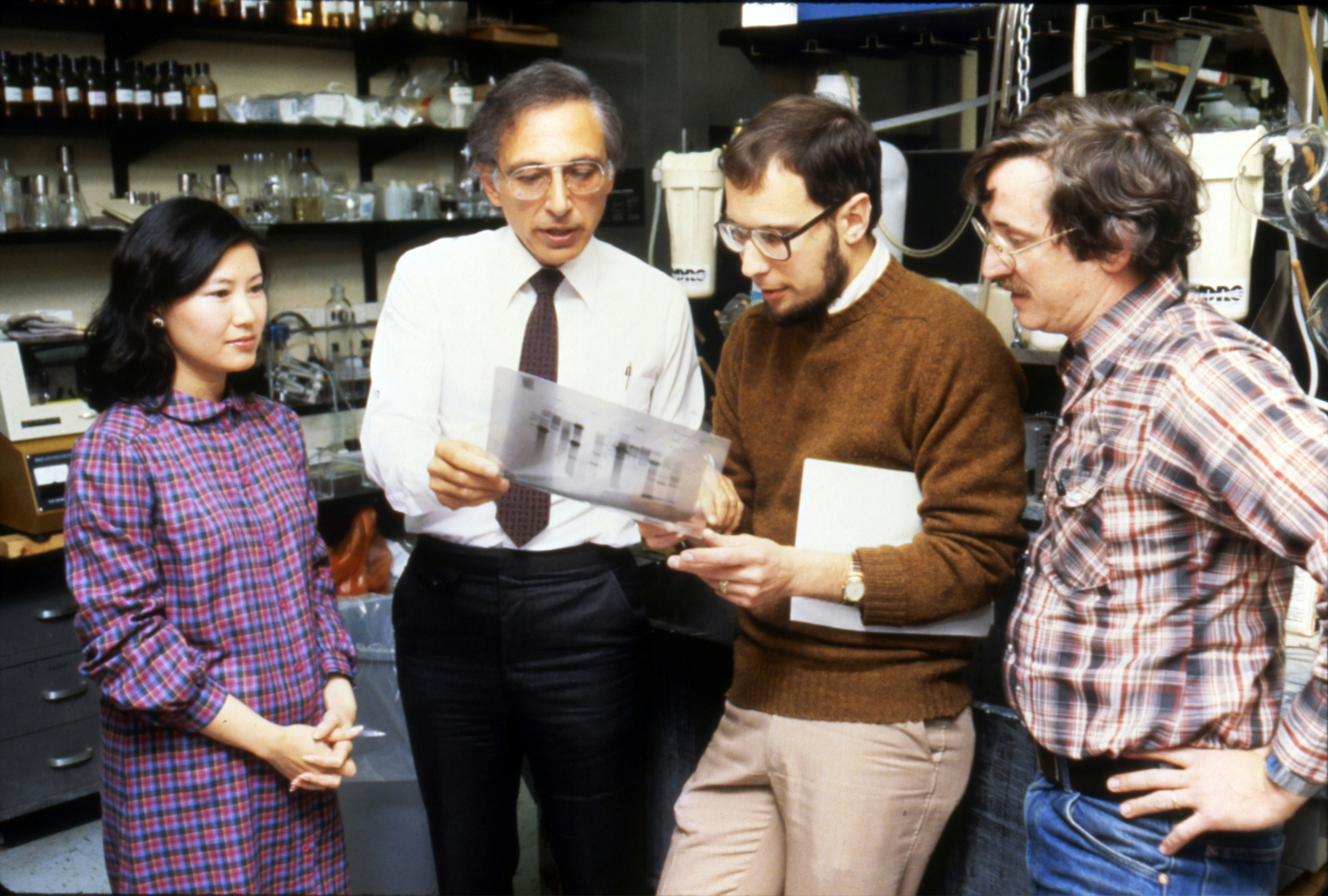 Robert Charles Gallo (second from the left), former Biomedical Researcher. He is best known for his work with the Human Immunodeficiency Virus (HIV), the infectious agent responsible for the Acquired Immune Deficiency Syndrome (AIDS). He was the former Chief of Laboratory of Tumor Cell Biology at the National Institutes of Health. Dr. Gallo is talking with three colleagues (one woman and two men). 1980