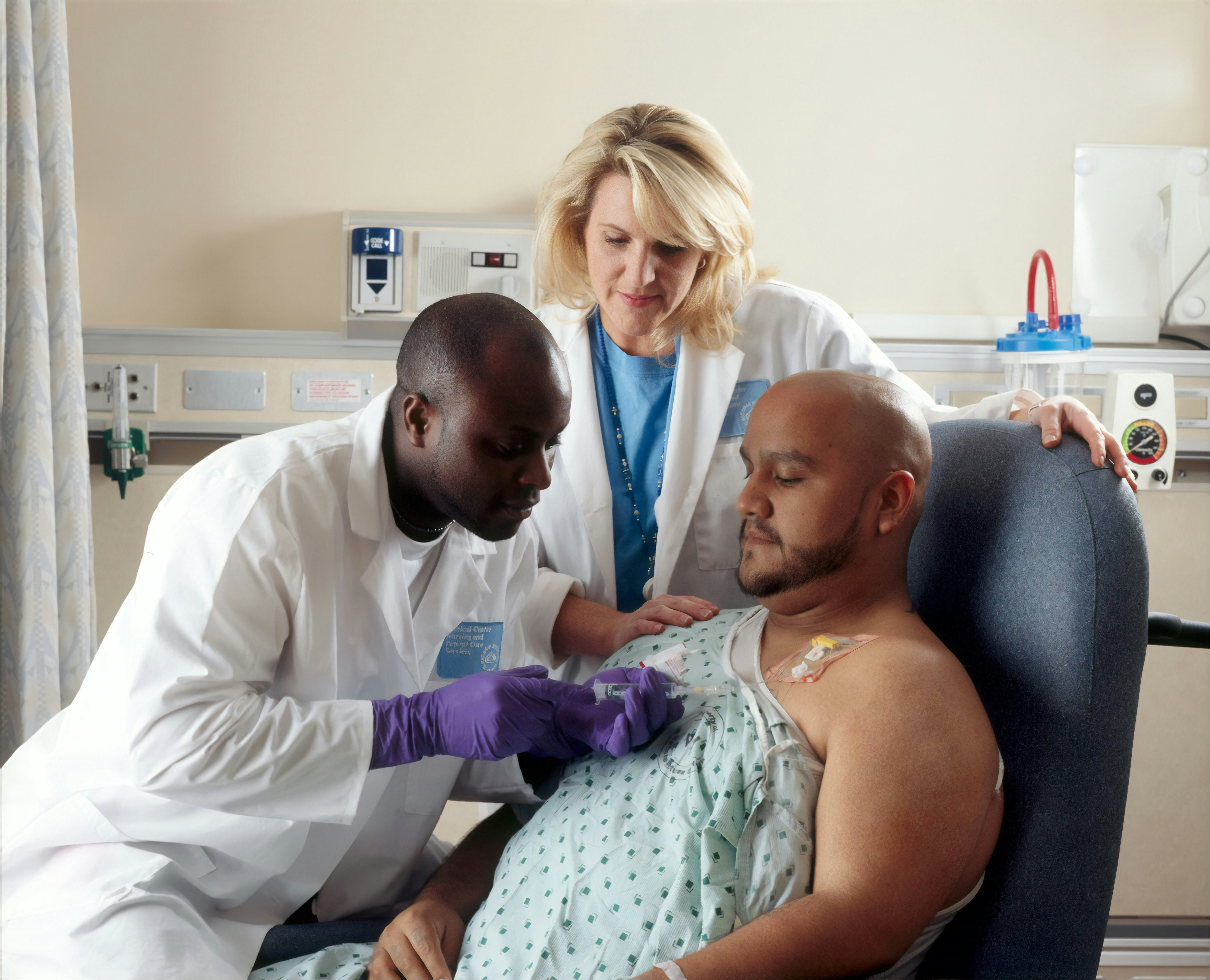 A Hispanic male patient receives Chemotherapy from a African-American Nurse through a port that is placed in his chest area. A caucasian female nurse looks on. 2010