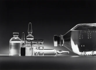 Glass medical vials and a large intravenous fluid bottle on a dark surface