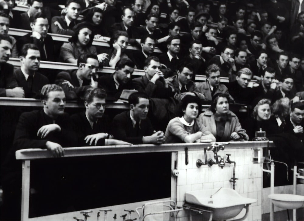 grayscale photography of people sitting on crowd chair