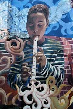 A mural depicting a young person playing a recorder. The background features swirling patterns and abstract forms, with clouds and smoke-like shapes surrounding the figure. The artwork incorporates vibrant colors and dynamic lines.