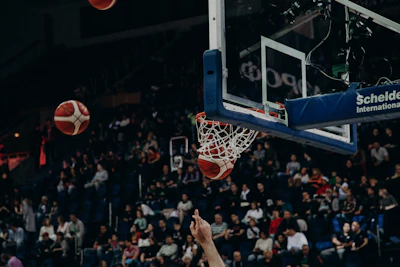 A dynamic shot of players leaping for a slam dunk under vibrant arena lights with a packed crowd in the background.