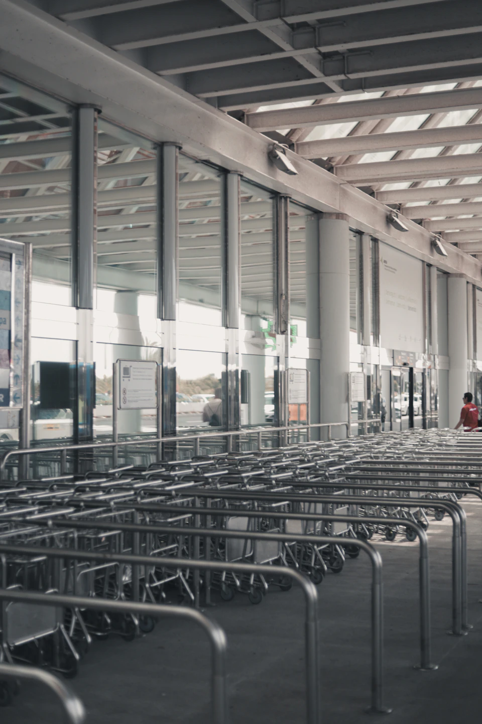 Large modern airport terminal with silver luggage carts in two parallel lines on floor