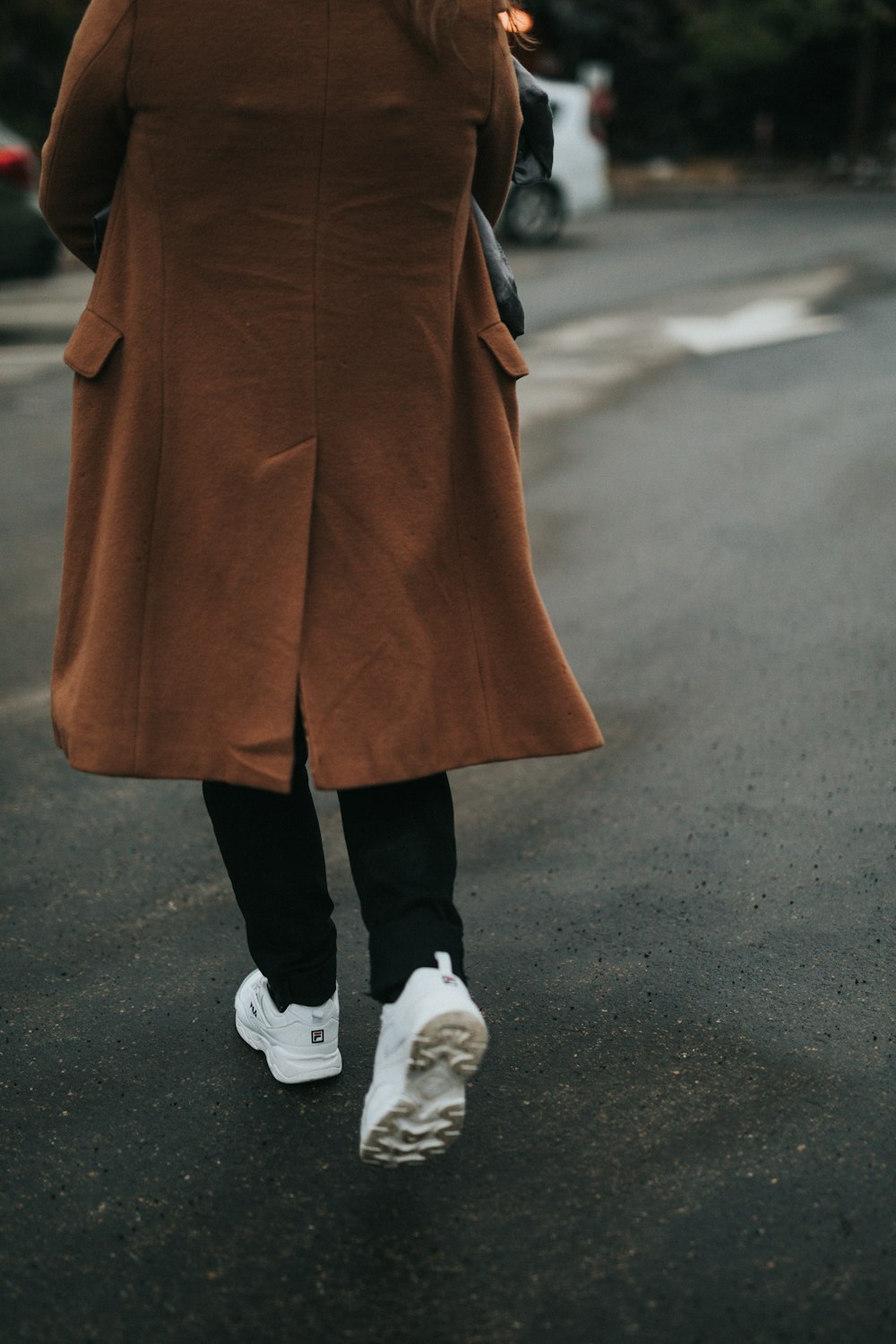 person wearing brown coat, black, pants, and white shoes
