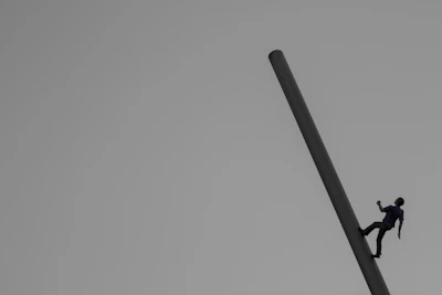 Tashi performing a powerful move atop a pole with soft neutral tones in the background.