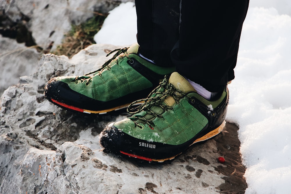 person in green-black low-top sneakers standing on top of rock