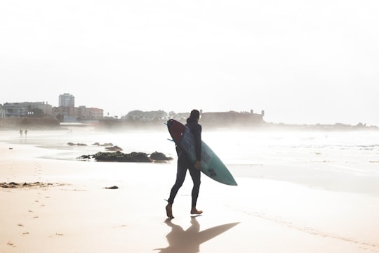 man carrying surfboard while walking towards the sea in Porto Portugal