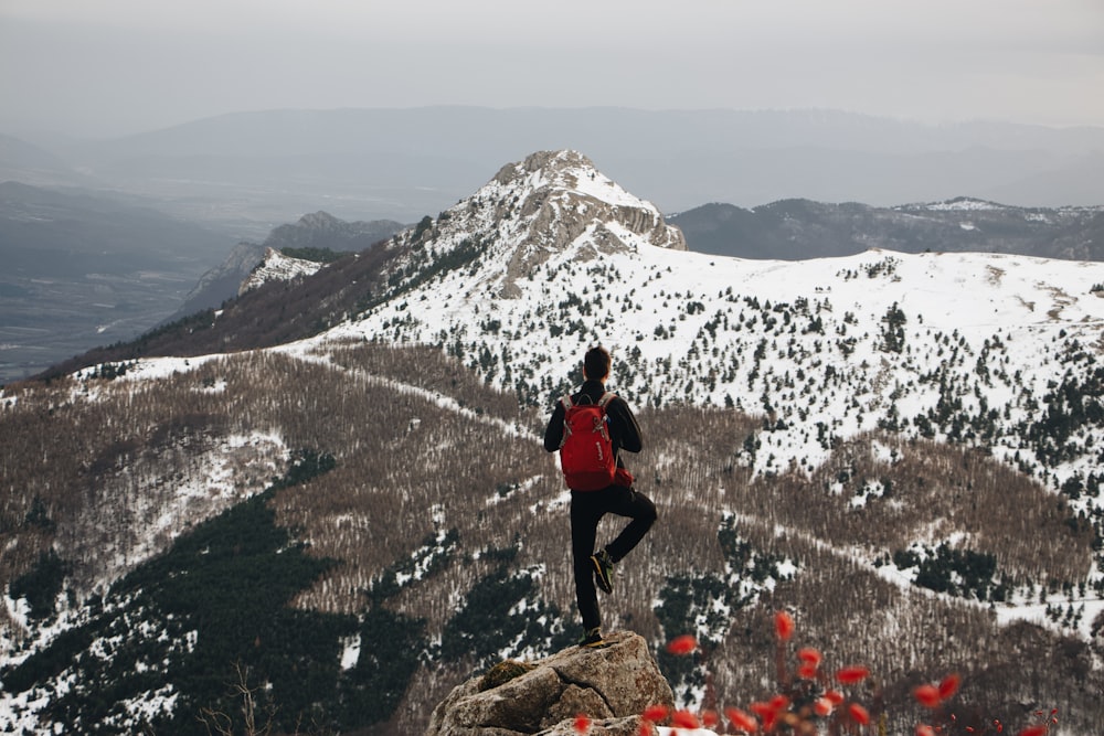 man standing on a mountain peak using one foot only