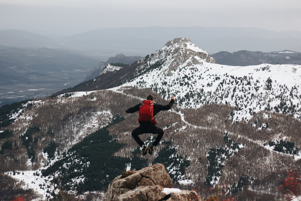 homem saltando na rocha de frente para as montanhas com neve