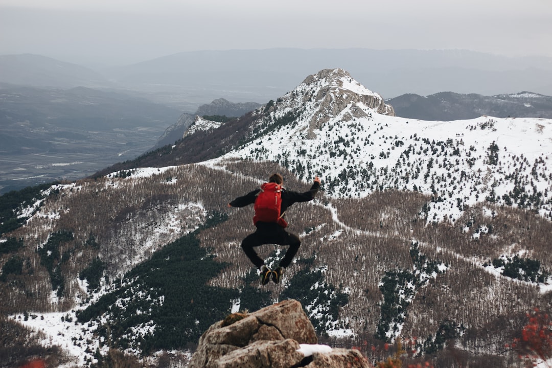 jumping man on rock facing mountains with snow