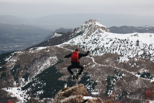 jumping man on rock facing mountains with snow in Céüse France
