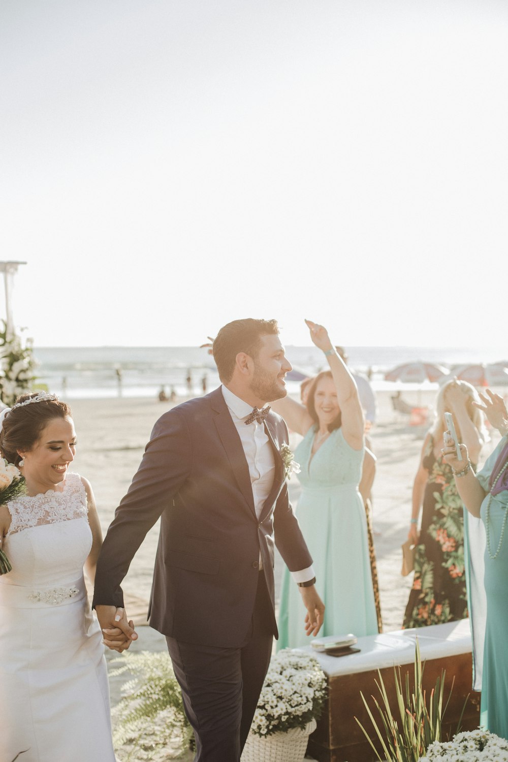 newly wed couple holding hands while standing surrounded with people viewing sea during daytime