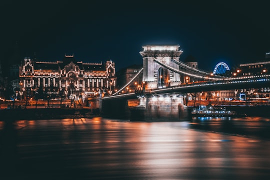 lighted bridge and building near sea during nighttime in Széchenyi Chain Bridge Hungary