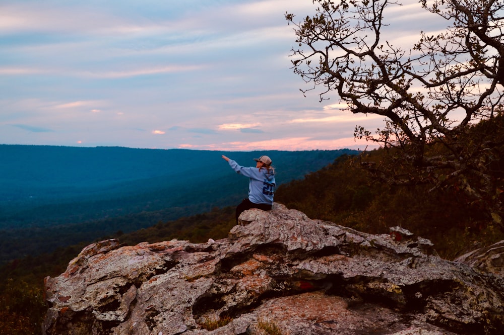 person sitting on stone cliff near tree during daytime