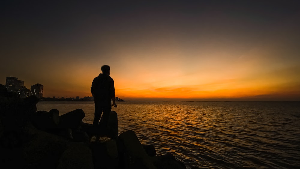 Fotografía de la silueta del hombre de pie en la orilla del mar durante la hora dorada