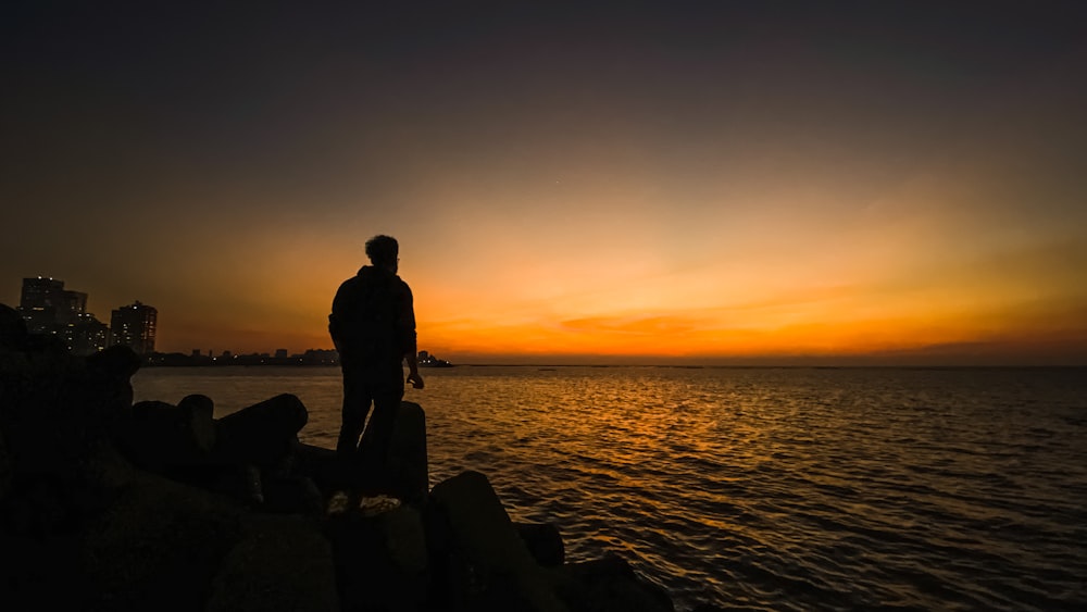 silhouette photography of man standing on seashore during golden hour