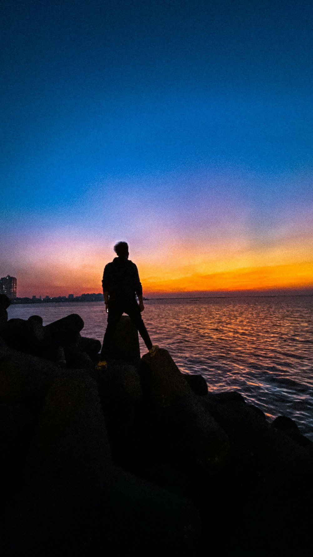 silhouette photography of man standing on seawall during golden hour