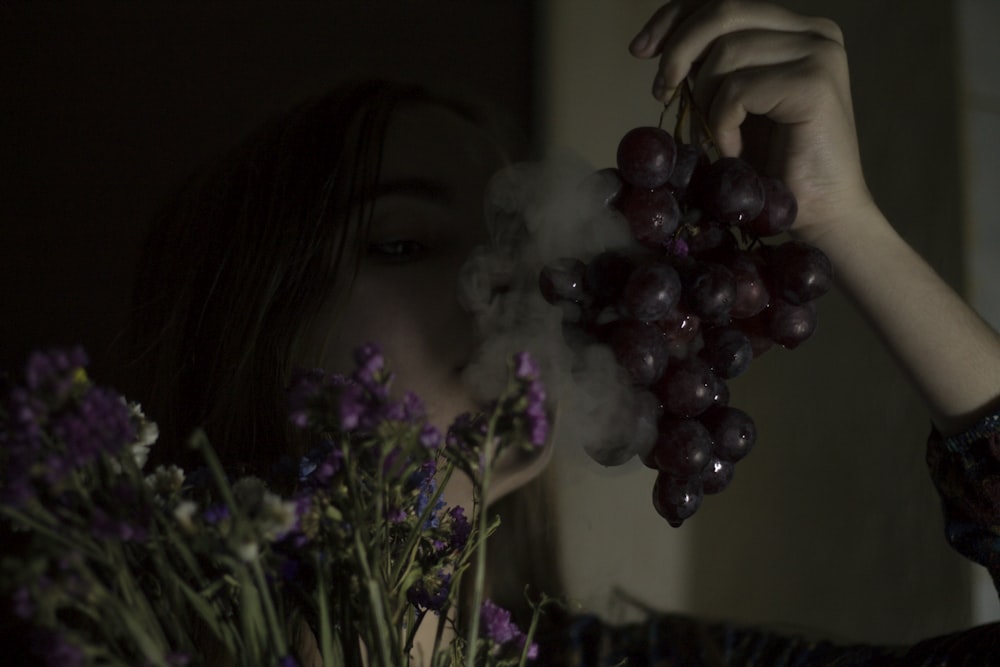 person holding purple grapes fruit and blowing white smoke on fruits
