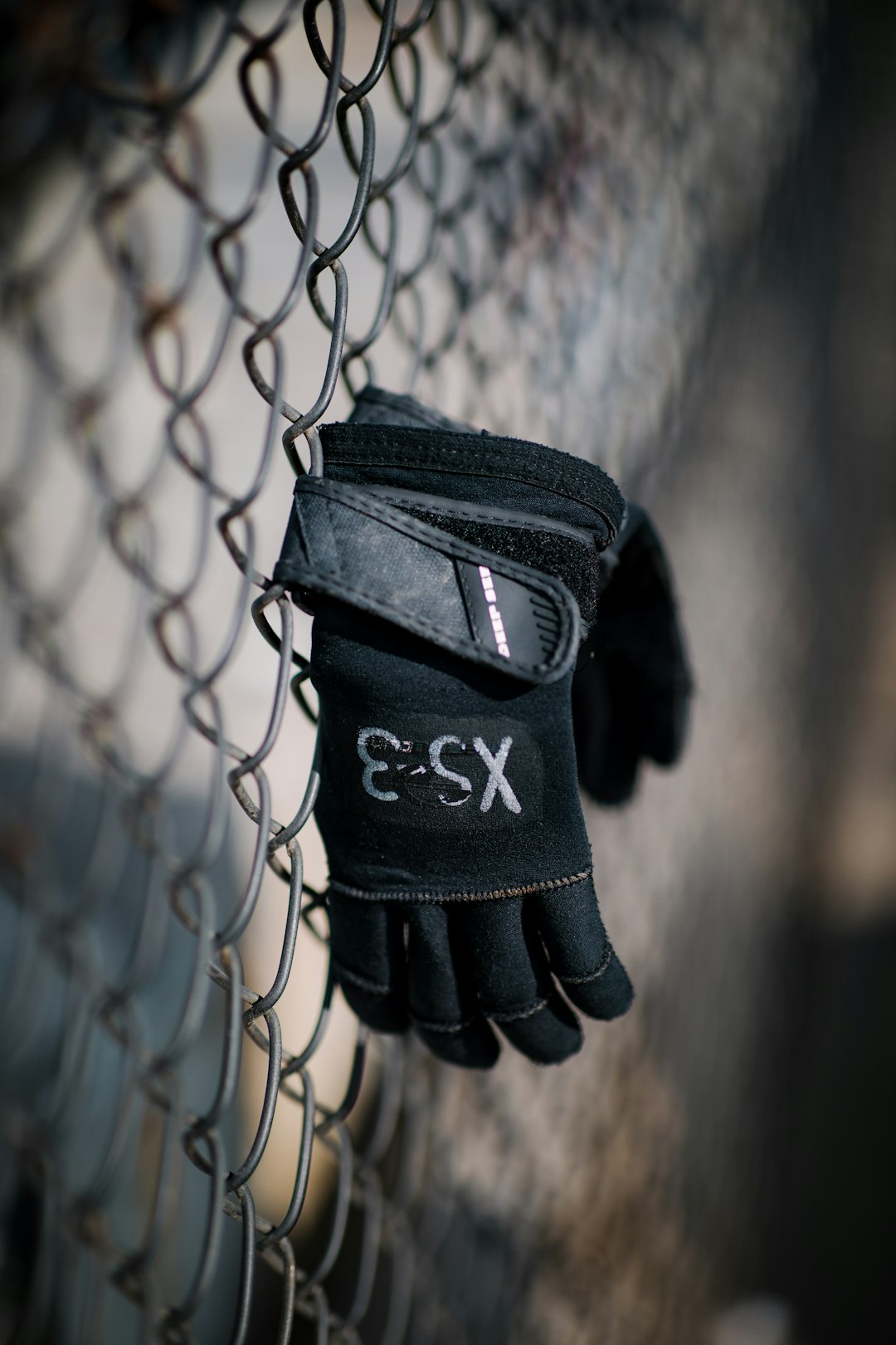 selective focus photography of pair of black gloves hanging on a wire fence