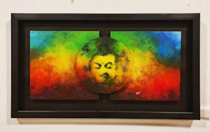 A colorful painting features a serene face within a circular cutout at the center of a vibrant background blending rainbow colors including red, green, blue, and yellow. The texture appears tactile with swirling patterns and abstract designs.