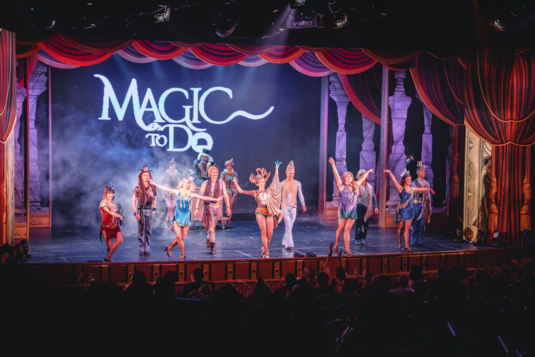 Performers on a lit theatre stage in front of red curtains