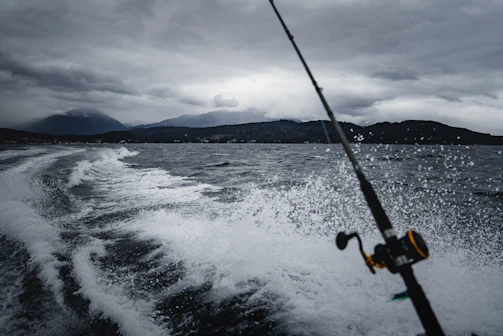 Fishermen casting lines from a boat with lush green mountains and waterfalls in the background.