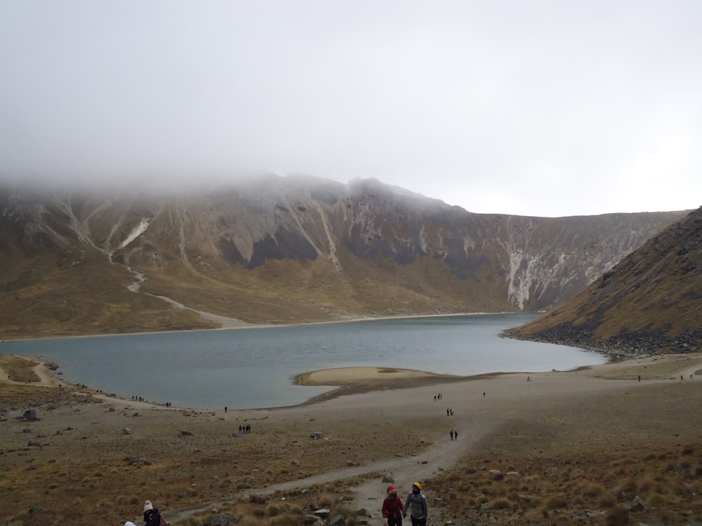 a group of people walking up a hill next to a lake