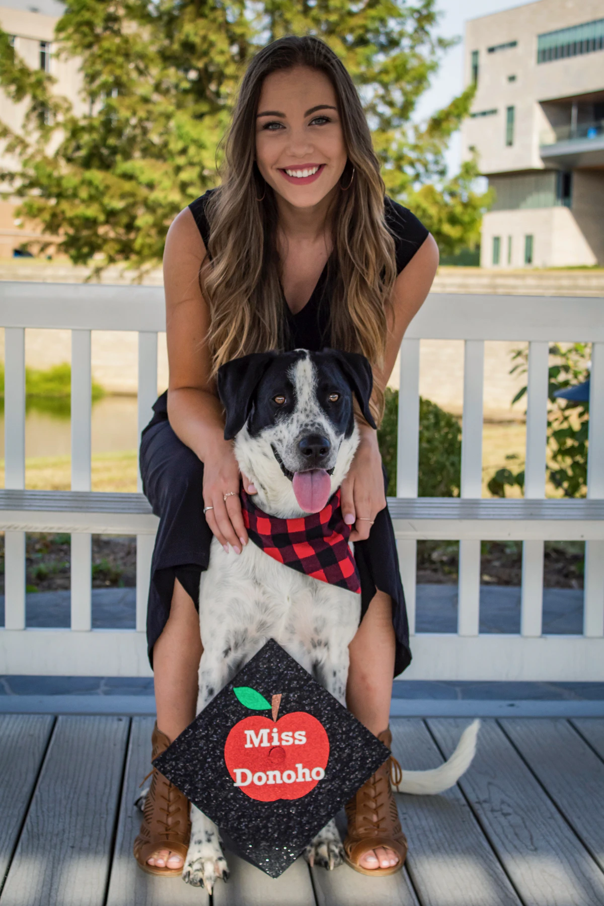 A young woman sitting on an outdoor bench with her arm around her dog
