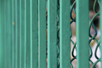 Close-up of a sturdy dark green metal fence with a natural backyard background.