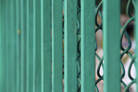 Close-up of a sturdy dark green metal fence with a natural backyard background.