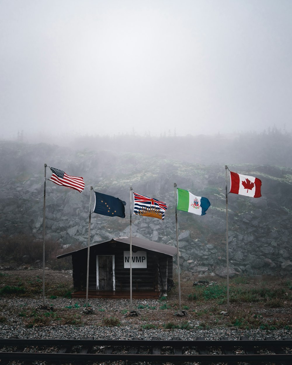 five assorted flags on poles by cabin during foggy weather
